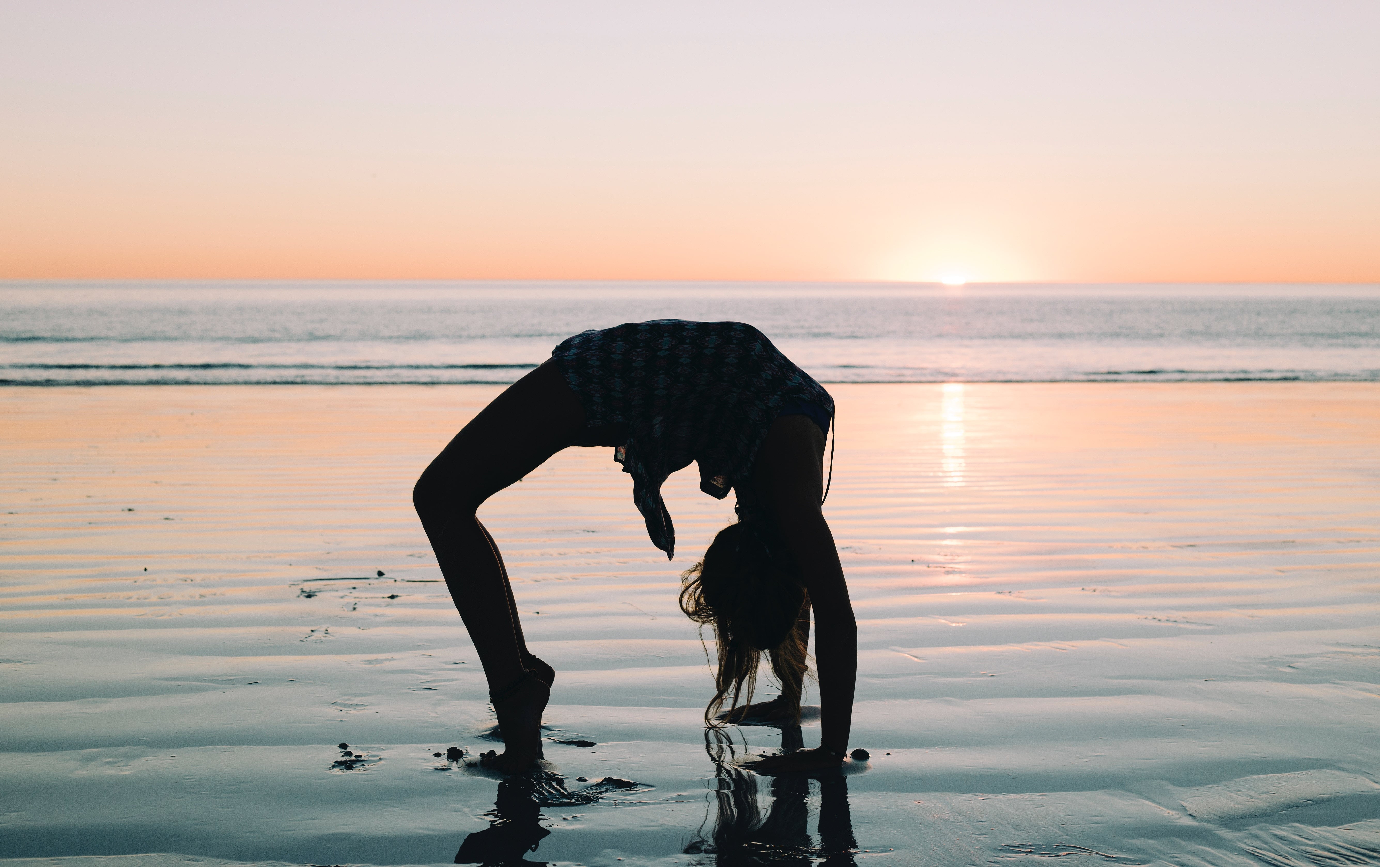 Woman doing wheel pose Urdva Danurasana during sunset on the beach